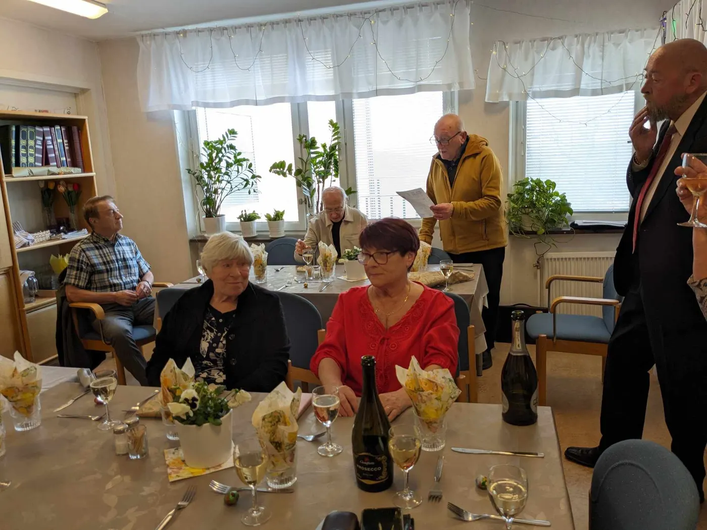 Gäster lyssnar vid bordet med utsikt mot fönstren