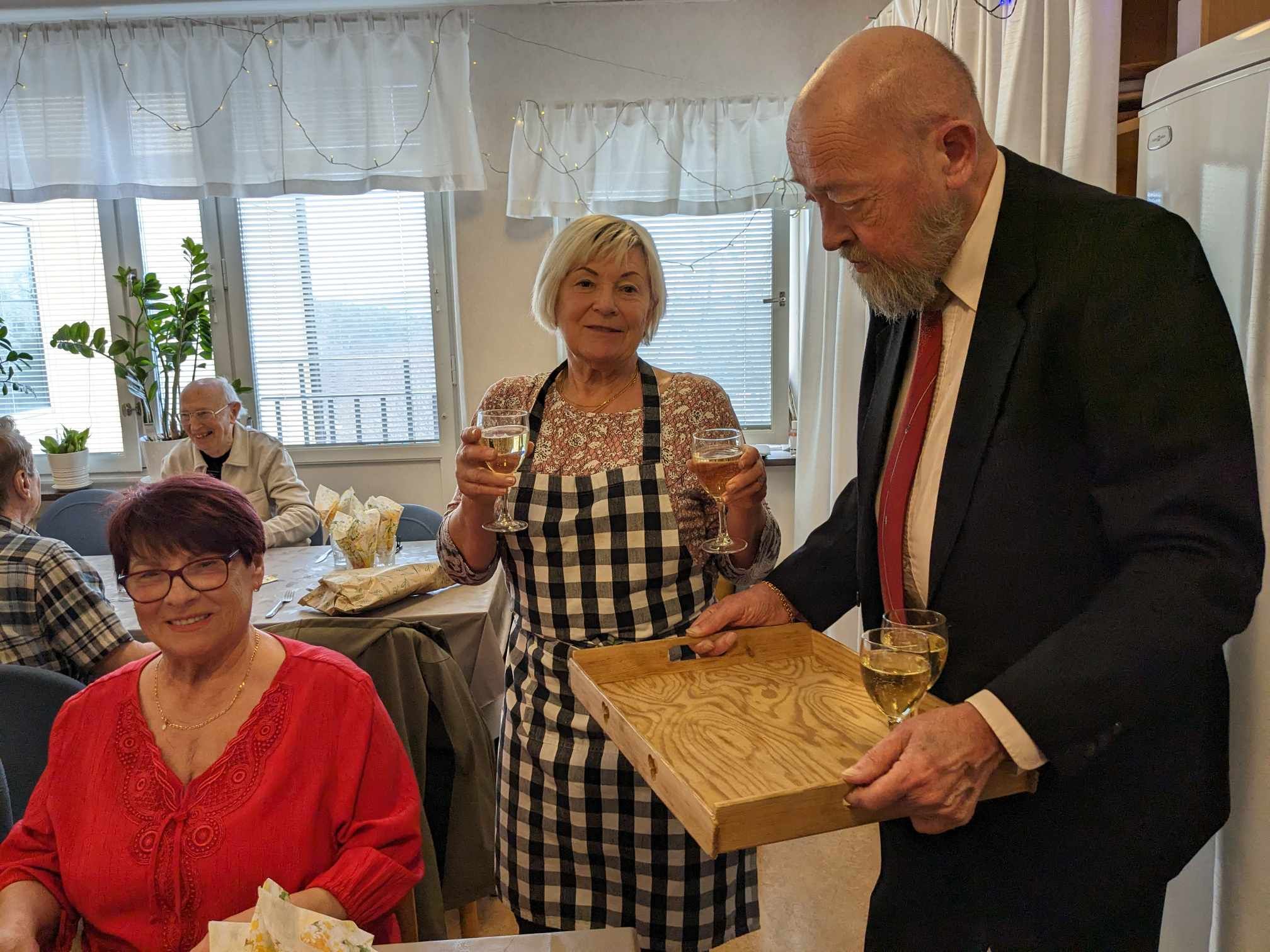 Värdinnan höjer glasen medan en gäst bjuder på bubbel från en bricka